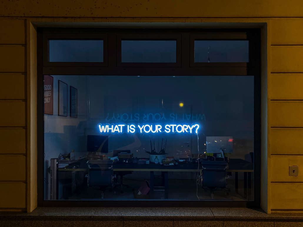 Neon sign in window reading what is your story?